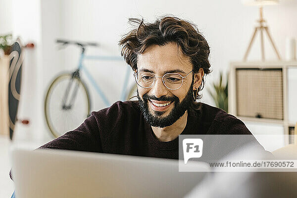 Smiling man wearing eyeglasses using laptop in living room at home