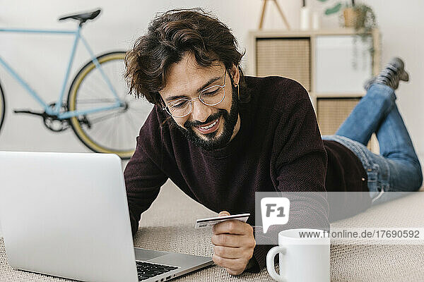 Smiling man making payment through credit card with laptop at home