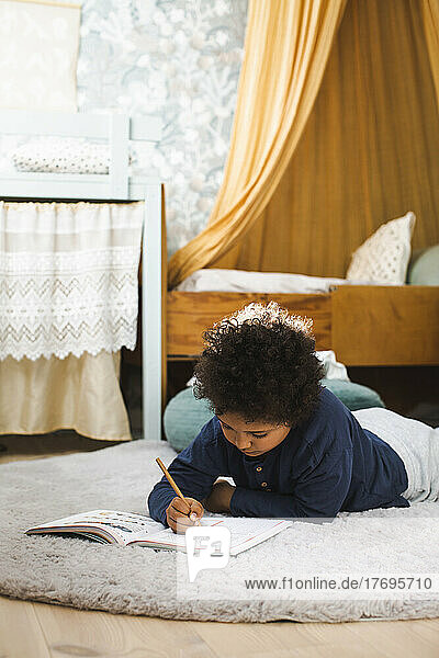 Junge macht Hausaufgaben  während er zu Hause auf dem Teppich liegt
