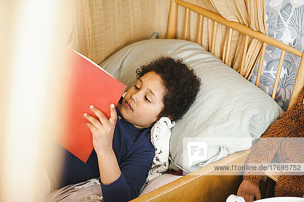 High angle view of boy reading story book while lying on bed at home