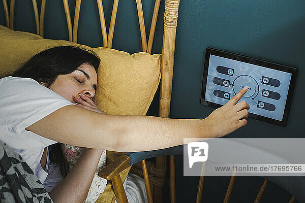 Frau gähnt  während sie ein Hausautomatisierungsgerät an der Wand im Schlafzimmer benutzt