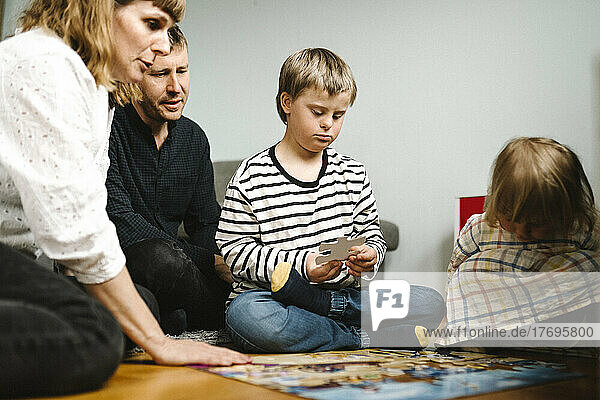 Junge mit Behinderung setzt Puzzleteile zusammen und sitzt mit seiner Familie zu Hause