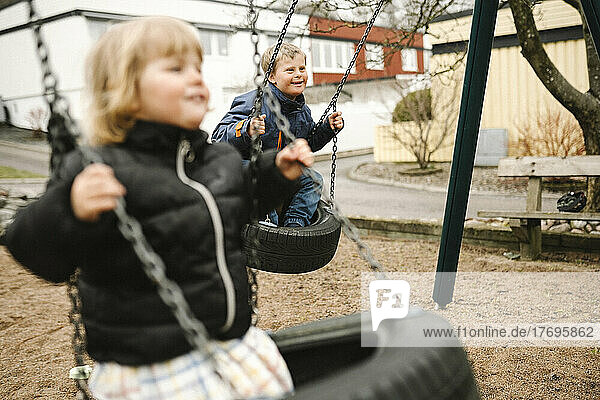 Verspielter Bruder und Schwester haben Spaß auf der Reifenschaukel im Park