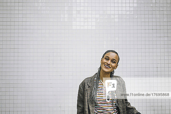 Porträt einer glücklichen jungen Frau mit geflochtenem Haar  die an einer weißen Wand steht