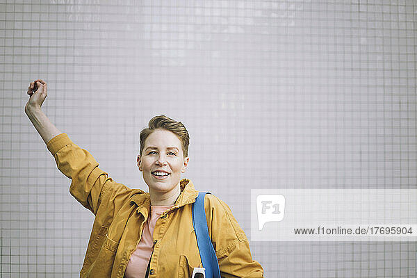 Porträt einer fröhlichen reifen Frau mit erhobener Hand an der Wand