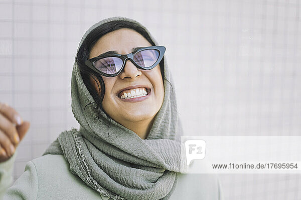 Fröhliche Frau mit Kopftuch und Sonnenbrille an der Wand
