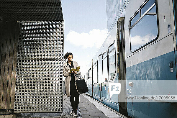 Geschäftsfrau  die ein Buch liest  während sie sich an eine Metallwand am Bahnhof lehnt