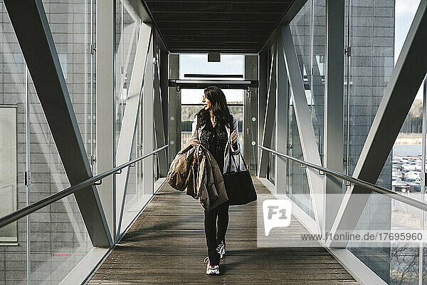 Geschäftsfrau schaut weg und hält eine Tasche  während sie auf einer Fußgängerbrücke geht