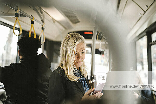Weiblicher Berufstätiger  der im Bus stehend ein Smartphone benutzt