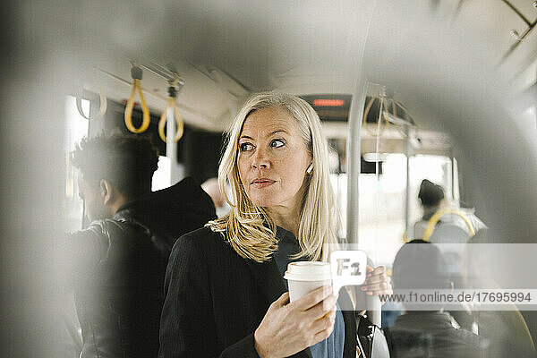 Nachdenkliche Geschäftsfrau mit Einwegbecher in der Hand auf dem Weg zum Bus