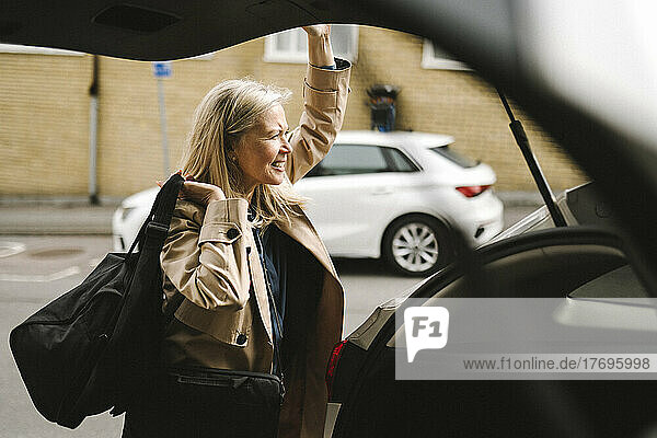 Geschäftsfrau trägt Gepäck  während sie den Kofferraum des Autos öffnet