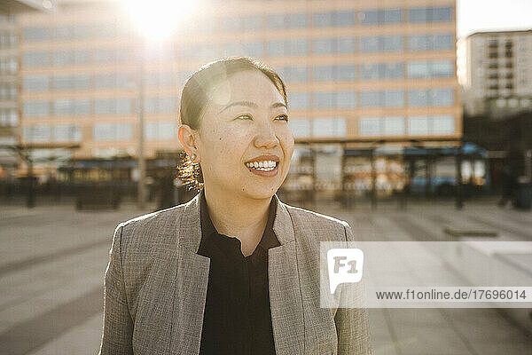 Lächelnde Geschäftsfrau mit Rückenlicht  die an einem sonnigen Tag wegschaut