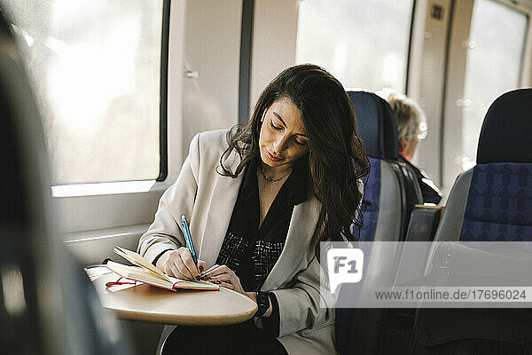 Businesswoman writing in diary while sitting by train window