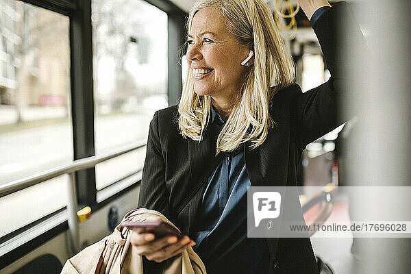 Happy businesswoman with smart phone travelling in bus