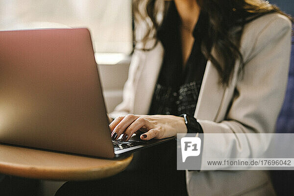 Mittelteil einer Geschäftsfrau  die einen Laptop benutzt  während sie im Zug pendelt