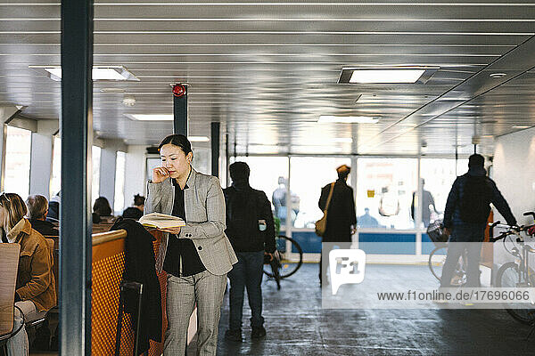 Businesswoman reading book while commuting through ferry