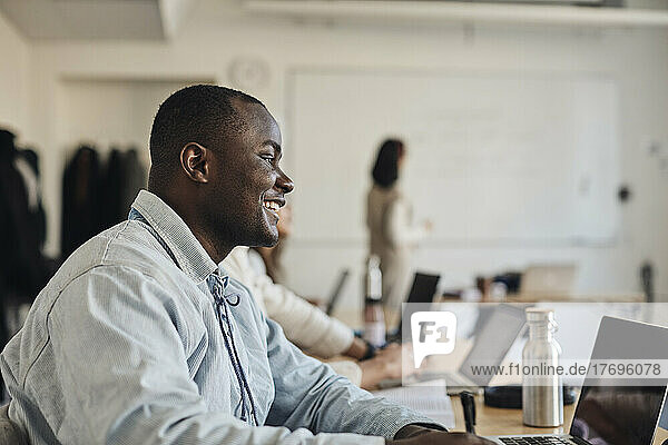 Seitenansicht eines lächelnden männlichen Schülers mit Laptop im Klassenzimmer