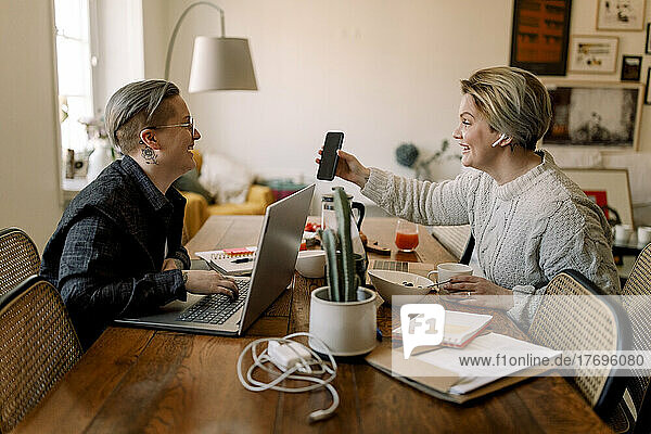 Glückliches lesbisches Paar  das sich bei der gemeinsamen Arbeit zu Hause ein Smartphone teilt