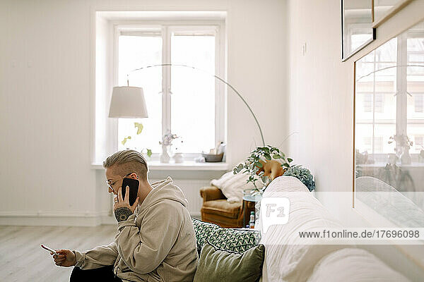 Seitenansicht einer Frau mit Schwangerschaftstestergebnissen  die über ihr Smartphone spricht  während sie auf dem Sofa im Wohnzimmer sitzt