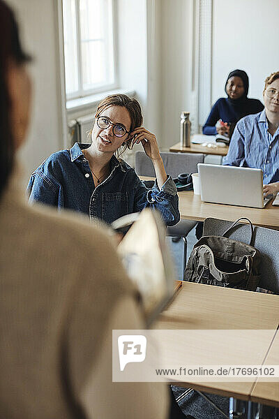 Female student talking to teacher during lecture in classroom
