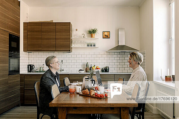Junges lesbisches Paar  das am Esstisch in der Küche sitzt und miteinander spricht