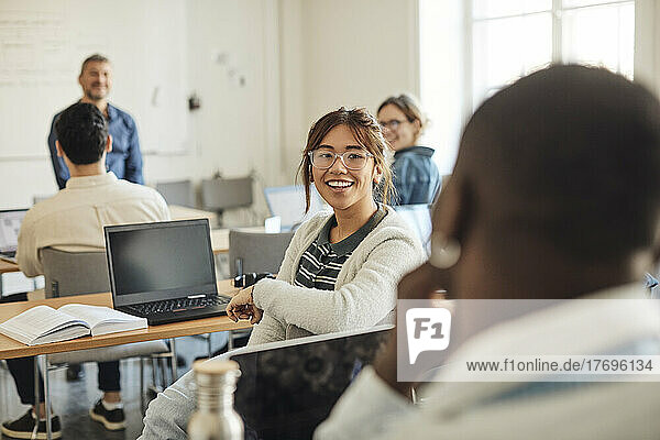 Smiling female student talking to male friend during lecture in classroom