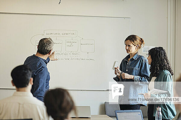 Männlicher Lehrer erklärt Schülern ein Diagramm  während er auf eine Tafel im Klassenzimmer zeigt