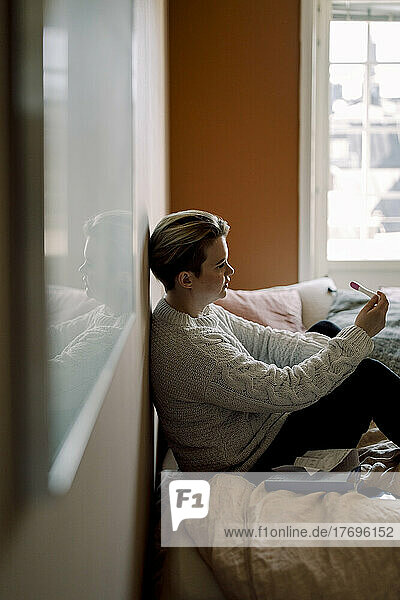 Depressive junge lesbische Frau mit Schwangerschaftstestergebnissen  die zu Hause auf dem Bett sitzt