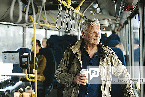 Nachdenklicher Geschäftsmann hält Einwegbecher beim Pendeln im Bus