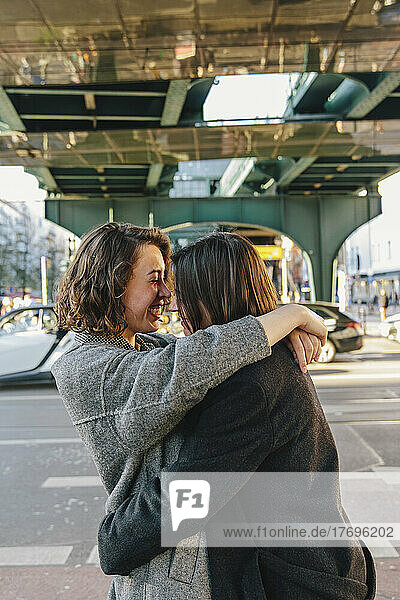 Fröhliches lesbisches Paar  das sich umarmt  während es auf der Straße unter einer Brücke in der Stadt steht
