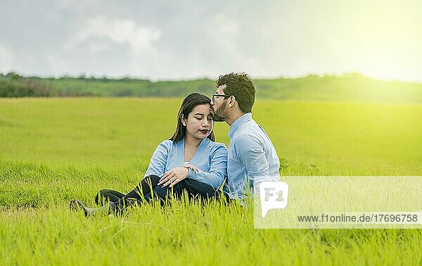 Ein verliebtes Paar sitzt im Feld und küsst sich auf die Stirn  Ein Mann küsst seine Freundin auf die Stirn im Feld  Romantisches Paar sitzt im Gras und küsst sich auf die Stirn