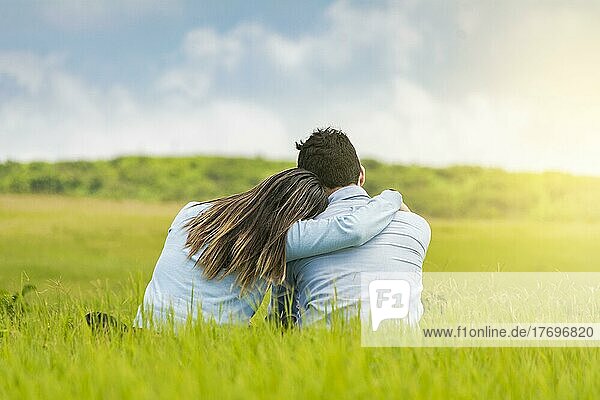 Romantisches Paar sitzt im Gras und umarmt sich von hinten  Rückansicht eines verliebten Paares  das sich im Gras umarmt  Ein verliebtes Paar sitzt im Gras und umarmt sich von hinten