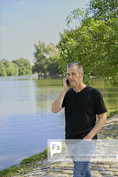 Älterer Geschäftsmann  der an einem See mit seinem Handy telefoniert