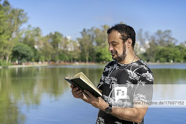 Älterer Mann  der an einem See liest und die freie Zeit an einem sonnigen Tag genießt