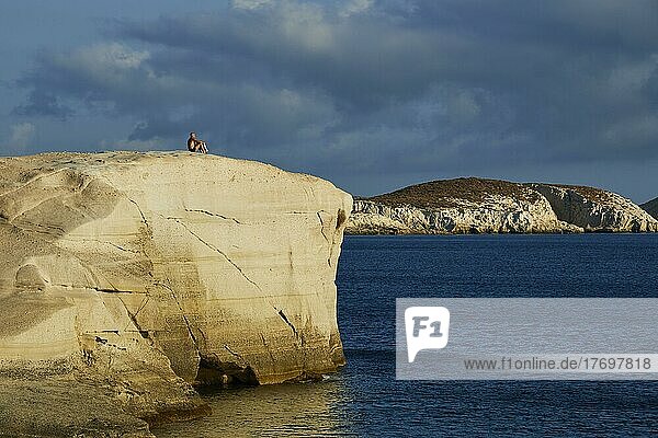 Morgenlicht  Tuffgestein  Mensch auf Tuff-Felsen  ruhiges dunkelblaues Meer  wolkiger Himmel  Sarakiniko Beach  Insel Milos  Kykladen  Griechenland  Europa