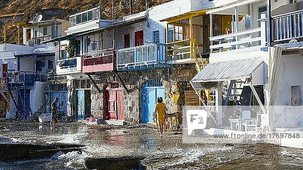 Bunte Bootshäuser  Gischt  Touristin in gelbem Kleid  Balkone  Holzhäuser  Klima  Golf von Milos  Insel Milos  Kykladen  Griechenland  Europa