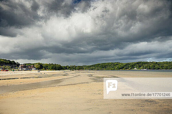Regenwolken ziehen über den Strand von Wassersleben an der Flensburger Förde. Das bewaldete Ufer im Hintergrund ist bereits dänisches Gebiet