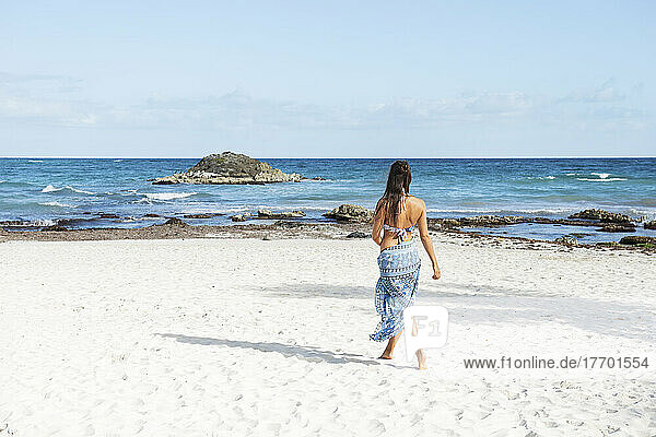 Young woman wearing bikini and sarong walking on beach