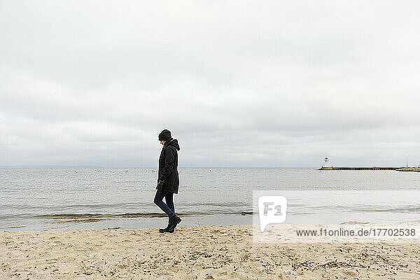 Woman in beanie and coat walking on beach