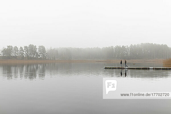 Young man and woman walking on pier at lake