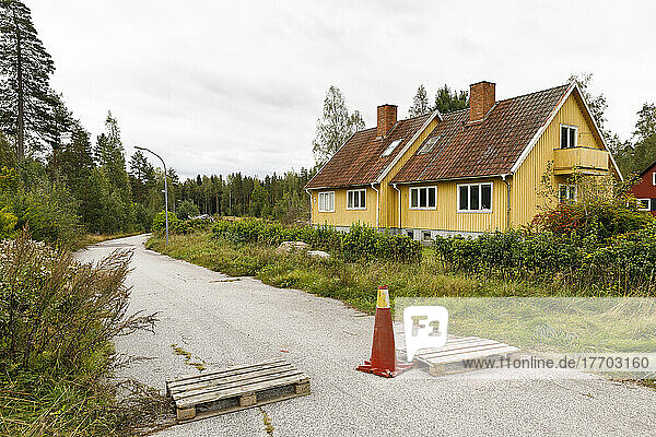 House by rural road blocked with traffic cone and wooden pallet
