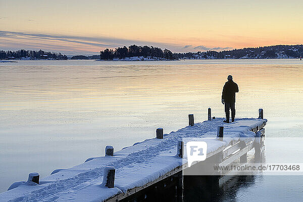 Man on snowy jetty on lake at sunset