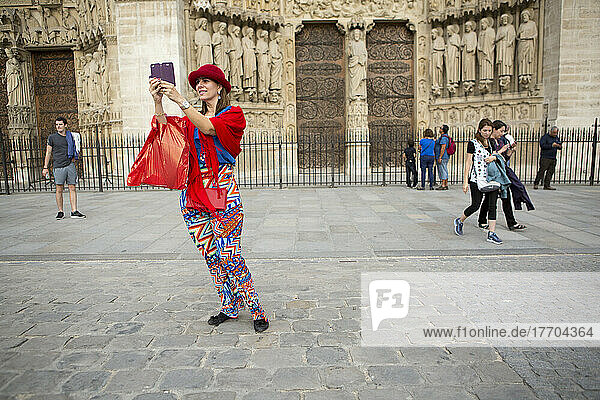 A woman in colourful clothes takes a self-portrait in front of the Notre Dame Cathedral in Paris  France; Paris  France