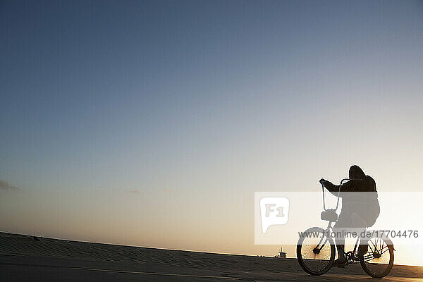Silhouette eines Radfahrers  der auf der Promenade neben dem Strand bei Sonnenuntergang fährt; Kalifornien  Vereinigte Staaten von Amerika