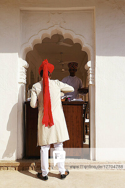 Ein Mann  der am Concierge-Schalter in einem geschwungenen Eingang des Ranvas-Palastes steht; Rajasthan  Indien