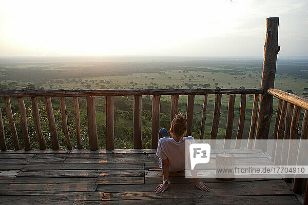 Ein Tourist ruht sich auf der Terrasse einer rustikalen Lodge aus und genießt die Sonne und die Aussicht auf die Ebenen des Queen Elizabeth National Park; Enganzi Game Lodge  Queen Elizabeth National Park  Uganda