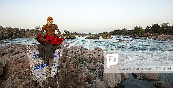 Sadhu holy man sitting on rocks on the Betwa River; Orchha  Madhya Pradesh  India