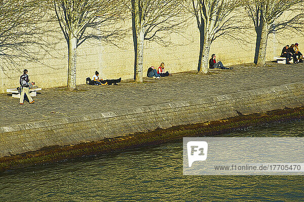 Sitzen an einer Wand im warmen Sonnenlicht entlang eines Flusses; Paris  Frankreich