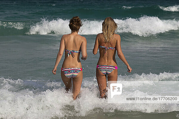 Girls in matching bikinis walk into the ocean.