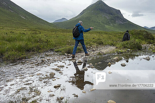 A hiker traverses a small stream along a trail in the Cuillin Mountains near Sligachan; Isle of Skye  Scotland